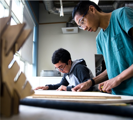 2 students wearing safety glasses engages with wood and other materials
