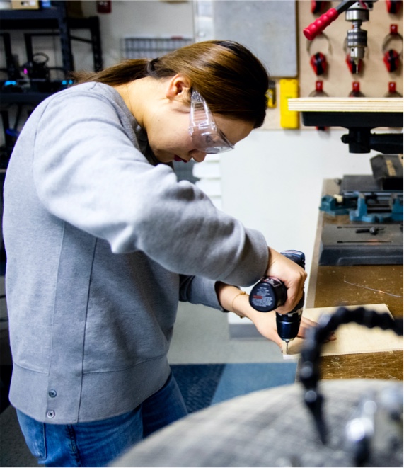 student wearing safety glasses drills into material 