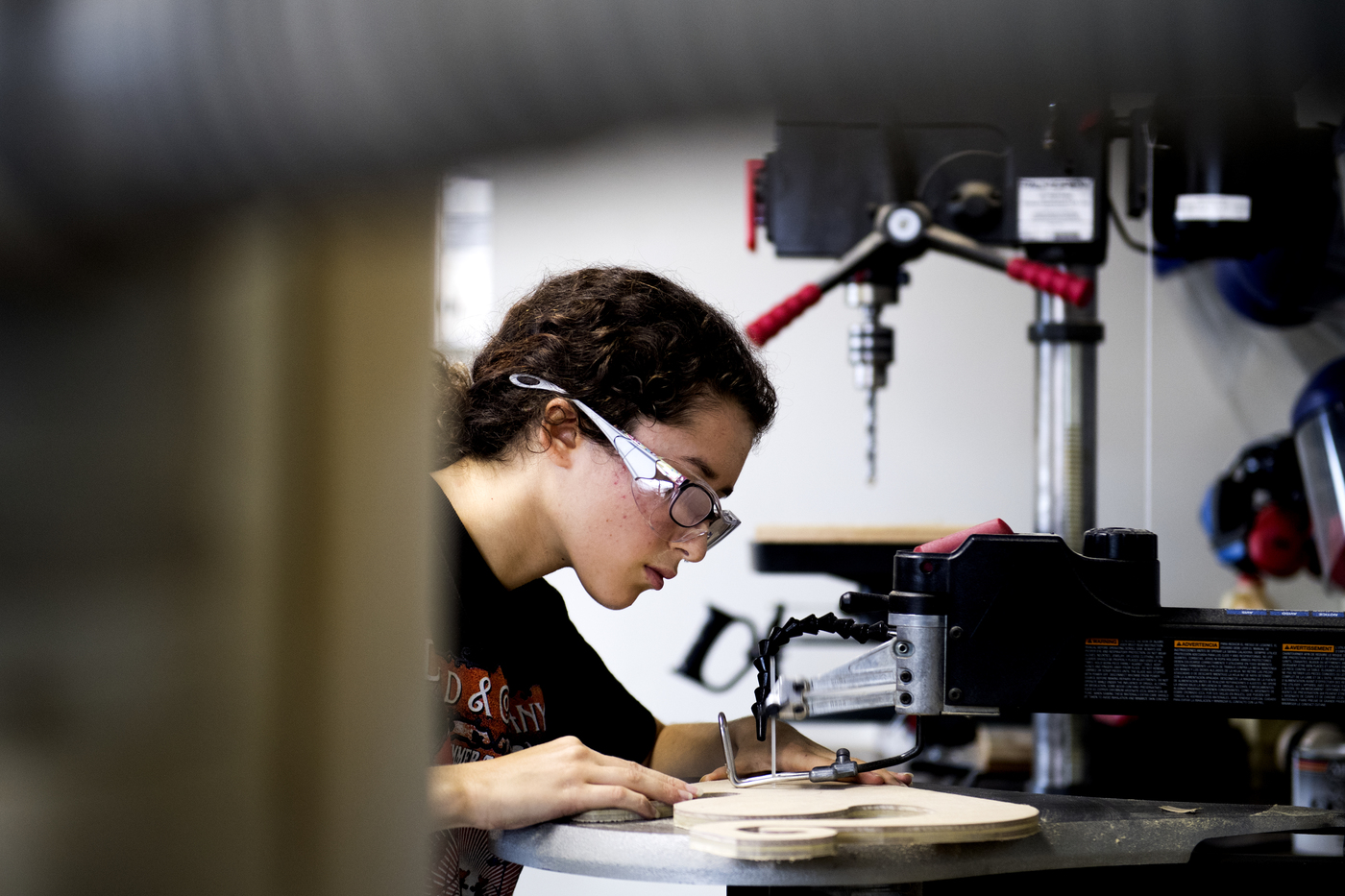 Student wearing safety glasses engages with woodworking equipment at a wood shop 