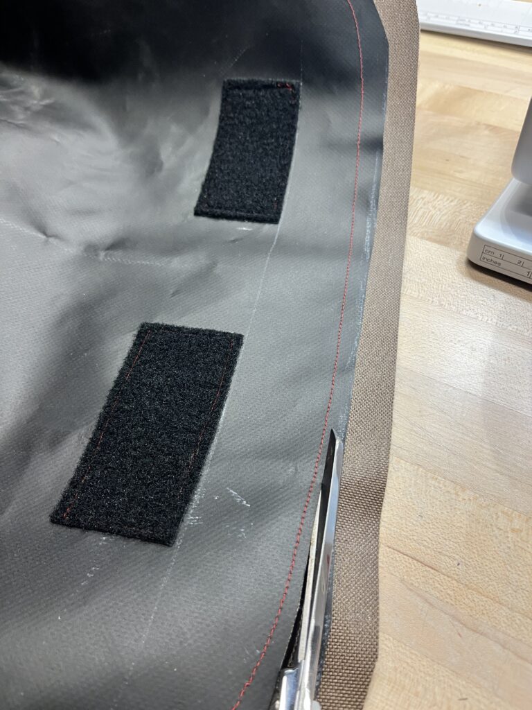 scissors cutting black and brown fabric next to red stitching