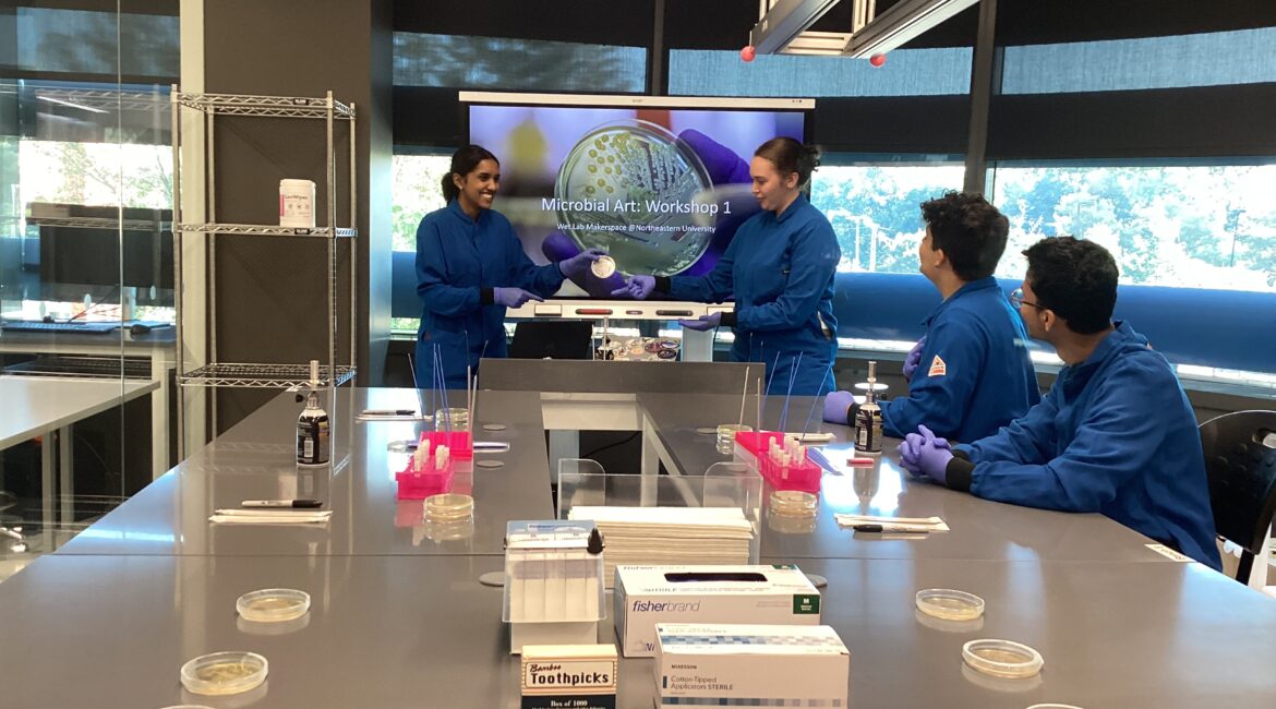 Students in blue lab coats take part in a Microbial Art workshop.